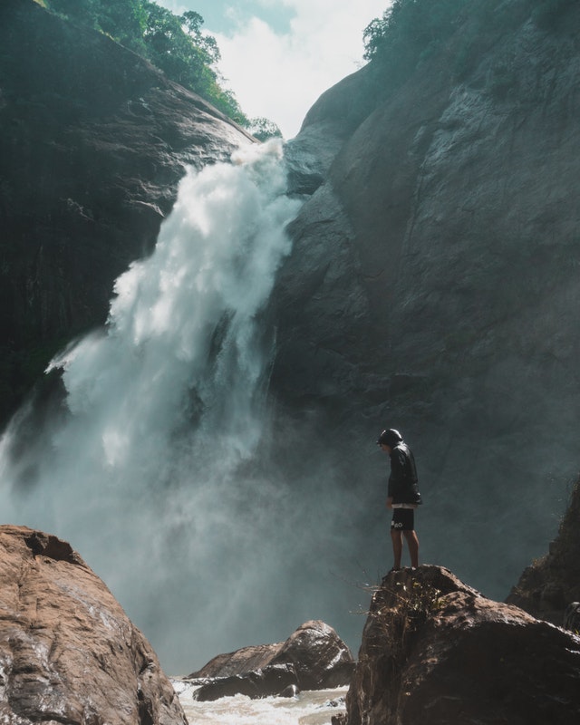 Man Standing On Brown Rock Cliff In Front Of Waterfalls 1047051