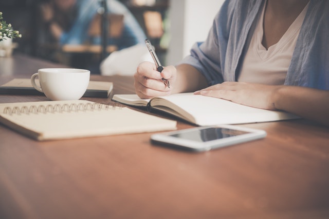 Woman Writing On A Notebook Beside Teacup And Tablet 733856